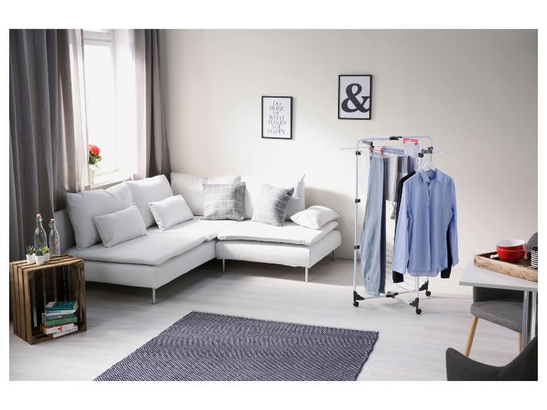 Witte hoekbank met kussens, houten krat met planten en een wasrek met kleding.