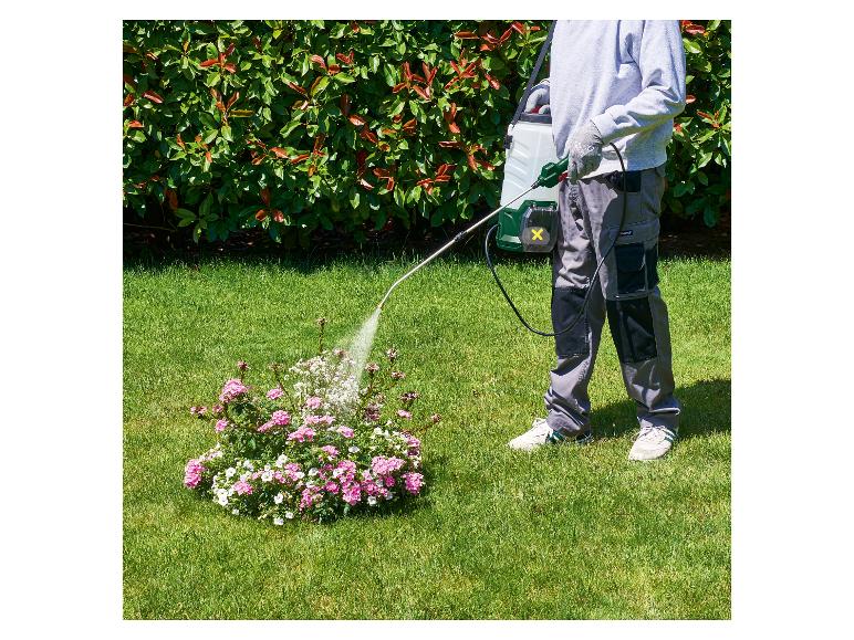 Man besproeit roze bloemen in de tuin met een Parkside rugsproeier.