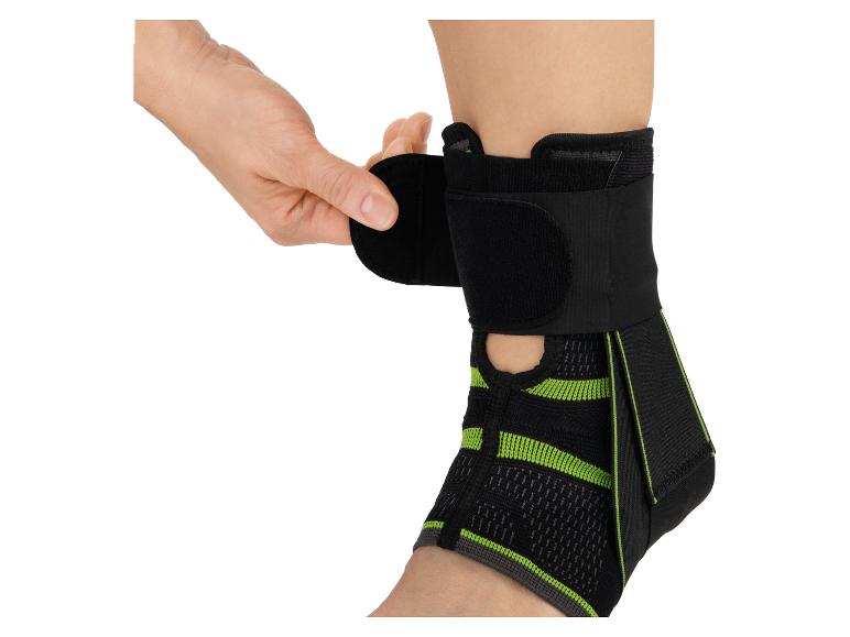 Een hand past een zwart-groene enkelbrace aan.