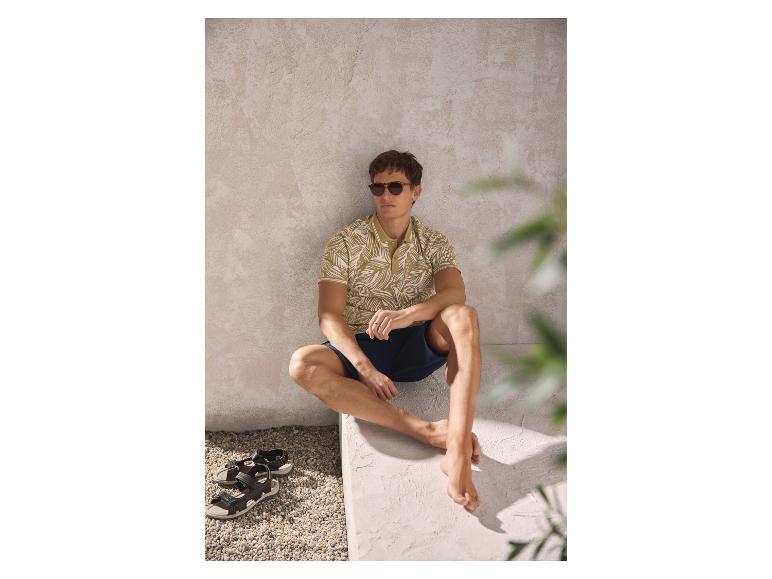 Man in bedrukt poloshirt en korte broek, zittend met sandalen ernaast.