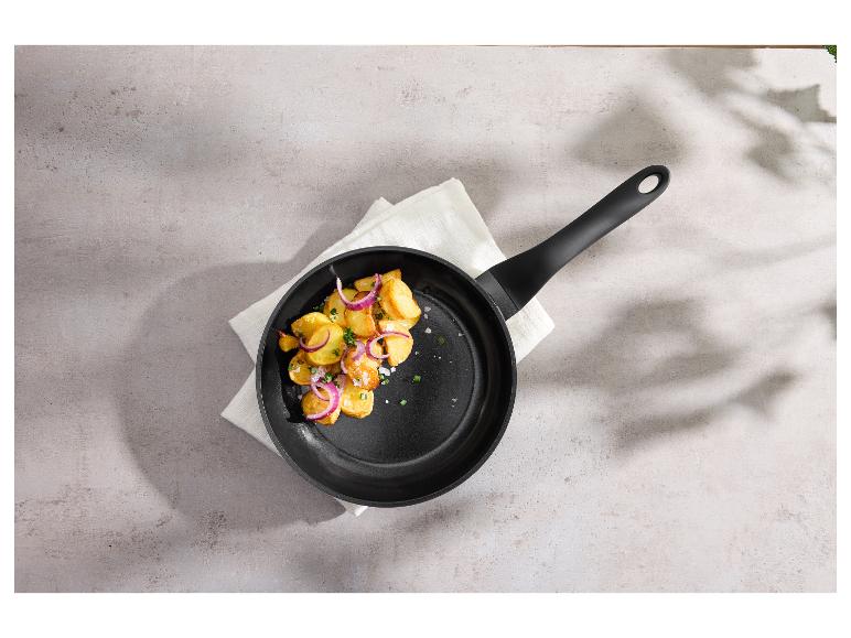 Koekenpan met gebakken aardappelen en rode ui op een wit servet.