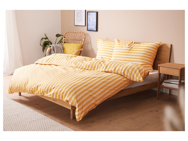 Een bed met gestreept geel beddengoed en een houten nachtkastje.