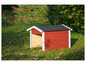 Een rood houten hondenhok met een zwart dak in een grasveld met bladeren.