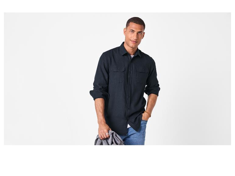 Man in donker overhemd en jeans, met een grijze jas.