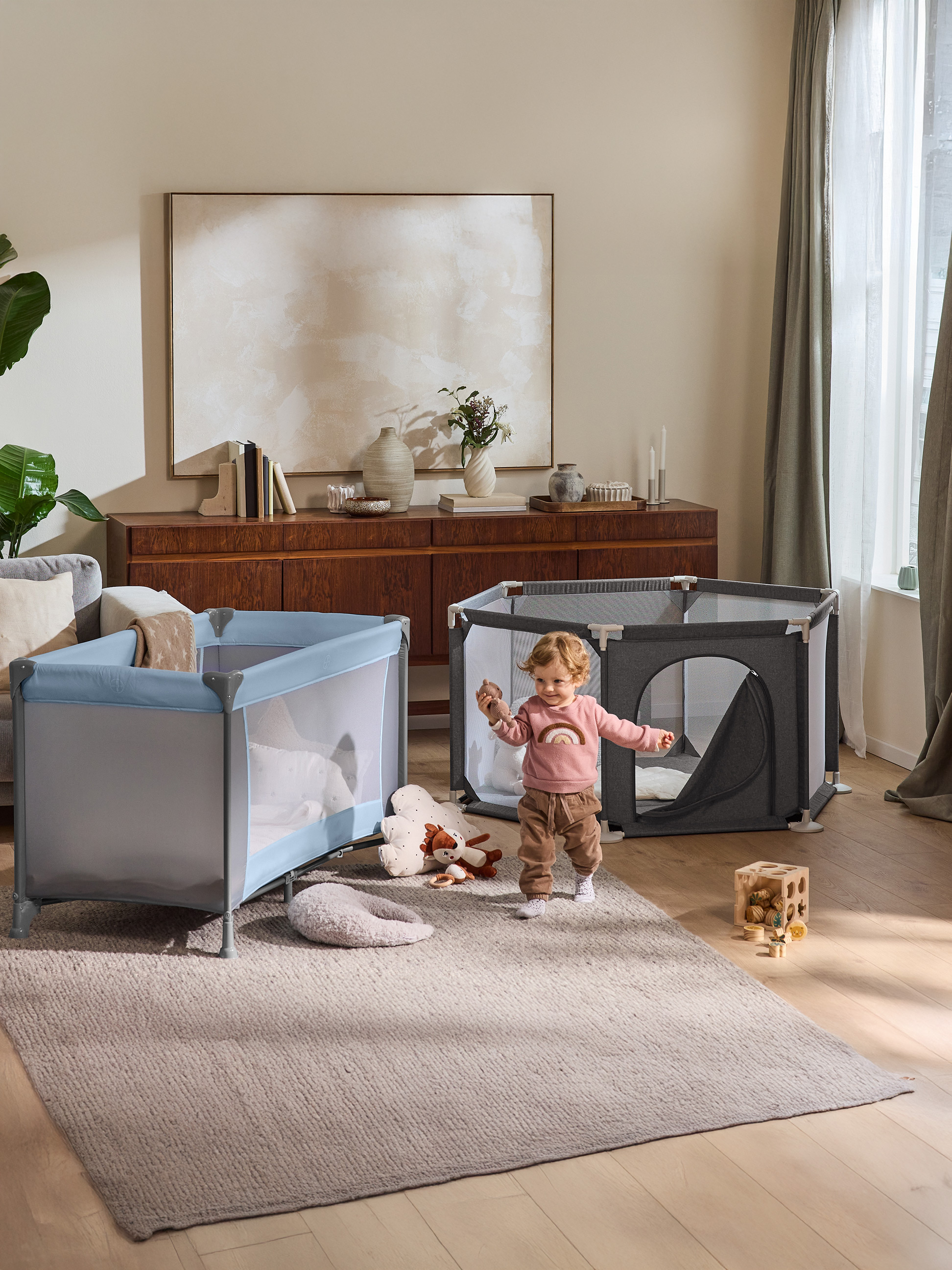 Peuter speelt in woonkamer met box en reiswieg.