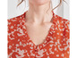 Close-up van een V-hals blouse met ruches, in een oranje print.