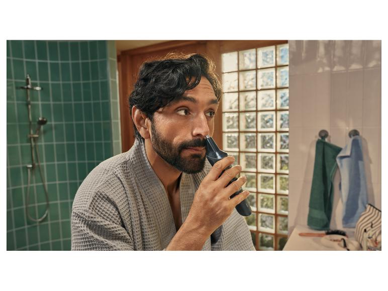 Man in grijze badjas gebruikt een neus- en oorhaartrimmer.