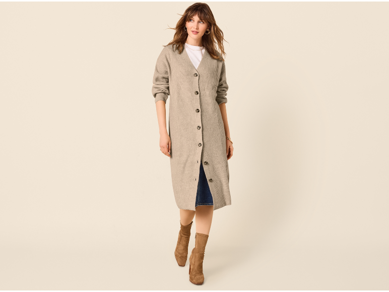 Vrouw in lang beige vest met knopen, wit T-shirt, spijkerrok en bruine laarzen.