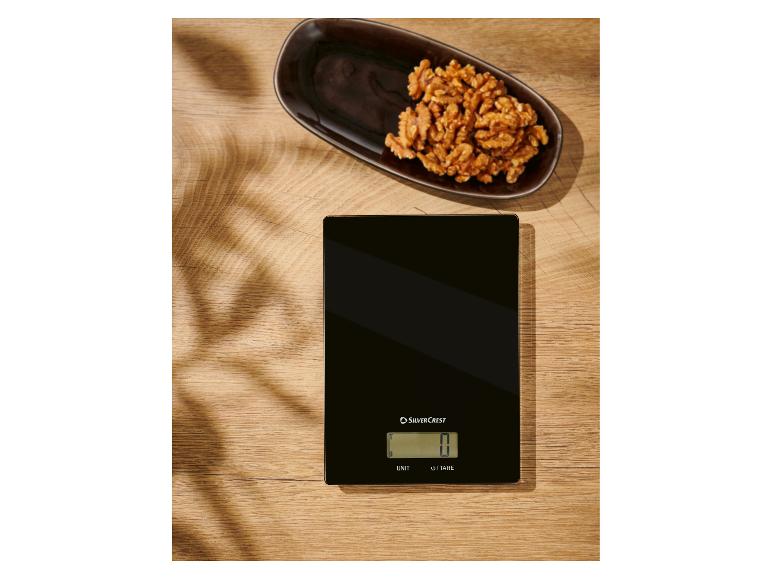 Een zwarte SilverCrest keukenweegschaal op een houten tafel met walnoten.