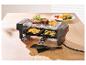 Raclette grill met biefstuk, aardappelen en courgette op een houten tafel.