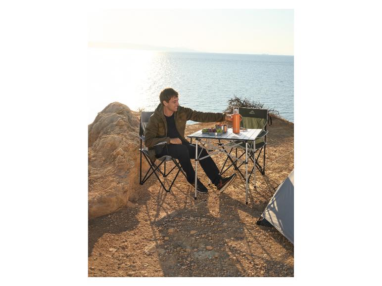 Man zit aan campingtafel met stoelen, naast tent, met uitzicht op zee.
