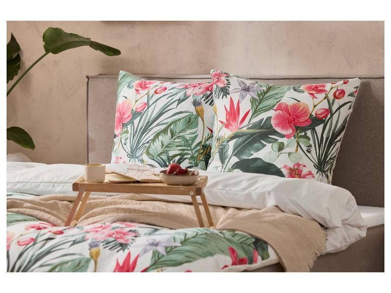 Bed met tropisch bloemig dekbedovertrek en kussens, ontbijtblad met koffie en fruit.