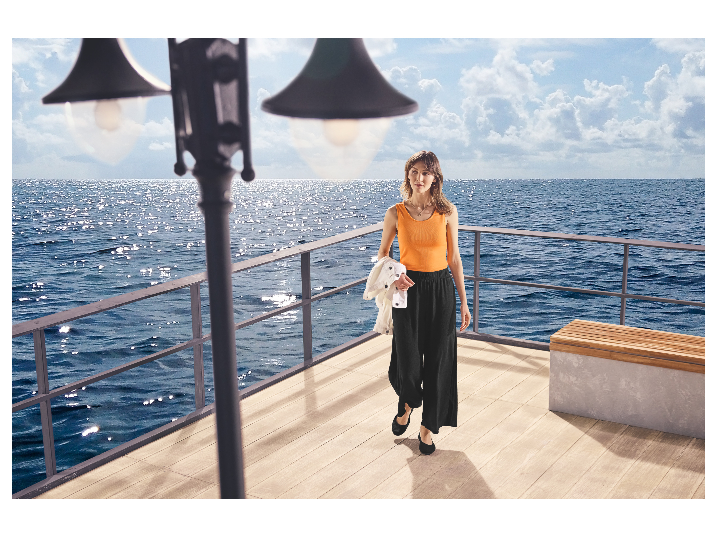 Vrouw in een ESMARA oranje geribbelde top op een houten dek met de zee op de achtergrond.