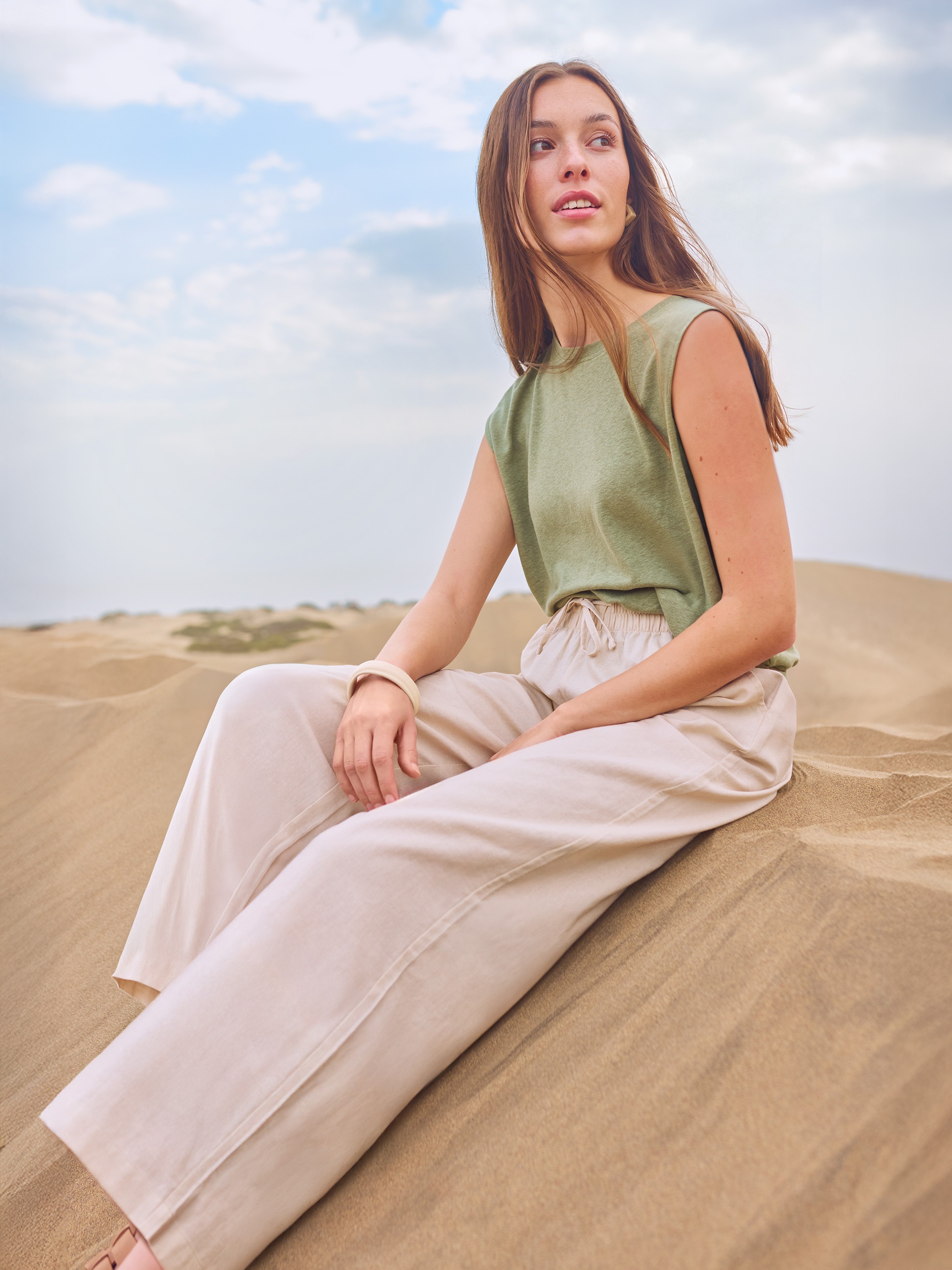 Vrouw in groen T-shirt en beige broek zittend in de zandduinen.
