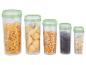Vijf doorzichtige containers met groene deksels, gevuld met pasta, maïs, koffie en haver.