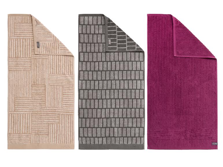 Drie badhanddoeken: beige met geometrisch patroon, grijs met baksteenpatroon en effen fuchsia.