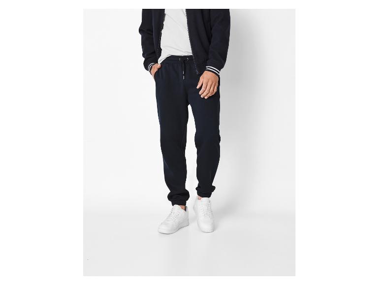 Man in marineblauwe joggingbroek en jack met rits, met witte strepen op de mouwen.