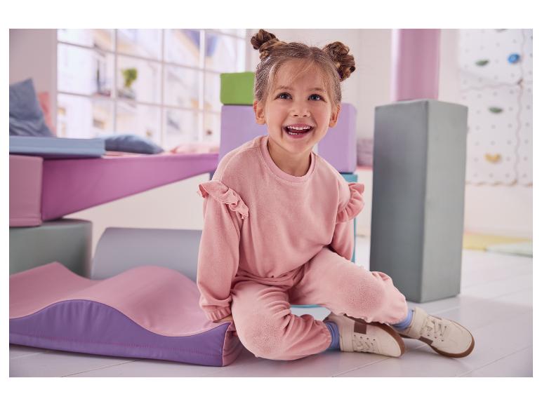 Blij meisje in roze set zit op de grond omringd door zachte speelmatten.