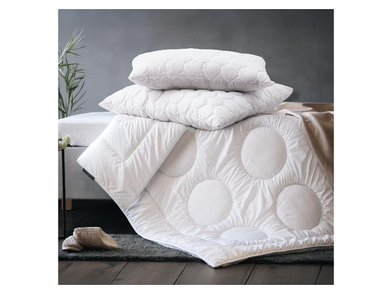 Wit gewatteerd kussen en dekbed op een bed met vloerkleed en pantoffels.