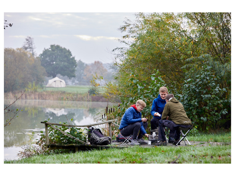 Drie mannen zitten op campingstoeltjes bij een meer met een tent op de achtergrond.