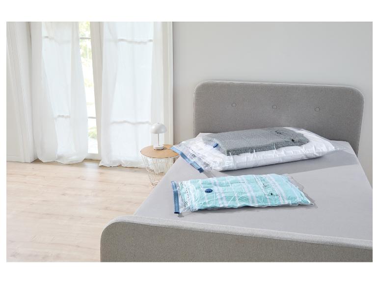 Vacuüm opbergzakken op een bed in een slaapkamer, één met een kussen en deken, de andere met handdoeken.