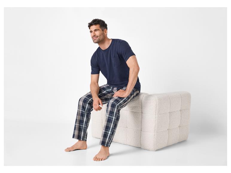 Herenpyjama: donkerblauw T-shirt en geruite broek, zittend op een beige poef.