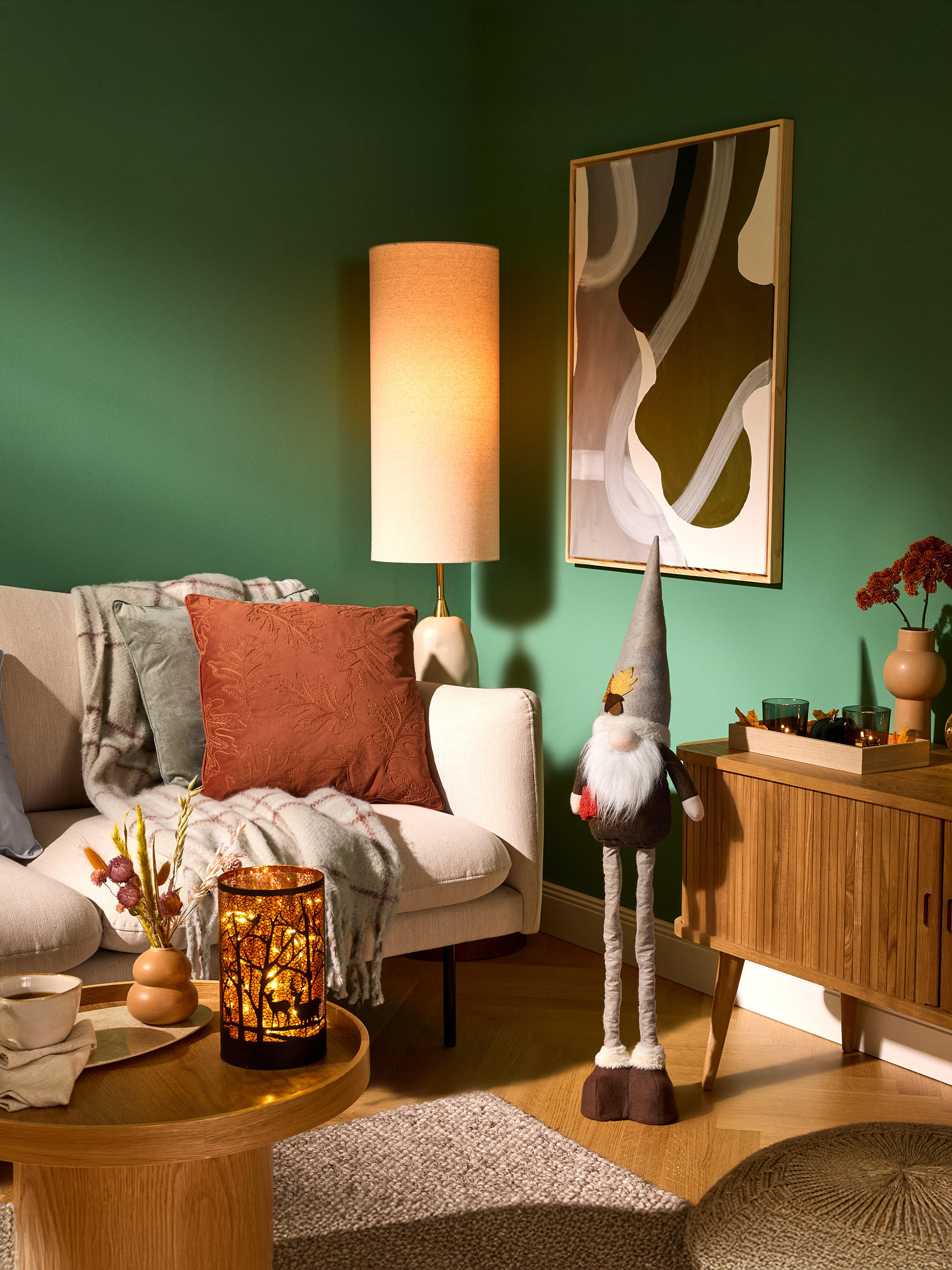 Gezellige woonkamer met groene muren, bank, vloerlamp en herfstdecoraties.