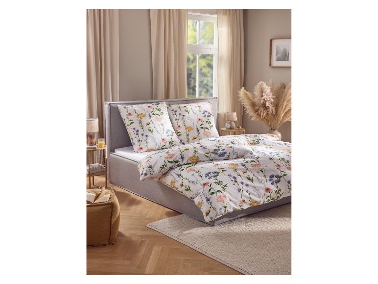 Slaapkamer met bed met grijs frame en bloemig beddengoed, naast een pluizig tapijt.