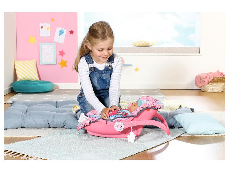 Meisje speelt met een BABY born pop in een roze autostoel op een kleed in een kinderkamer.