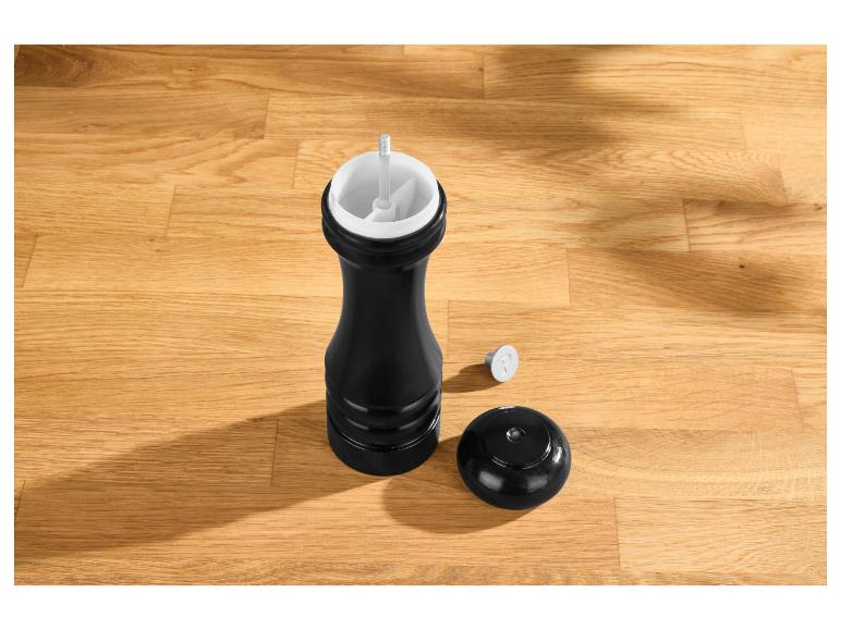 Zwarte pepermolen met deksel en een 'P' markering op een houten tafel.