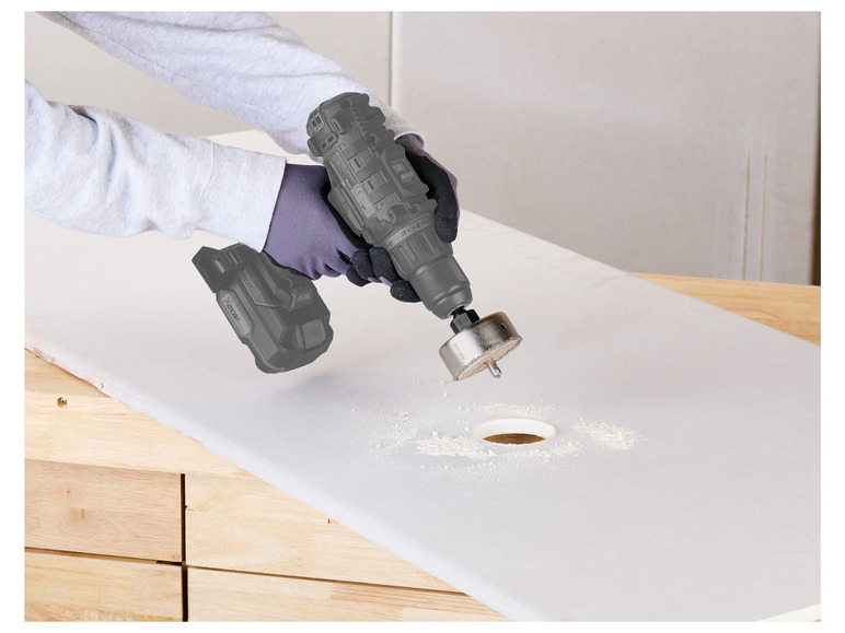 Een persoon gebruikt een X20V Max-boormachine met een gatzaag om een gat in een houten oppervlak te boren.