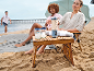 Draagbare blender en glazen met ijs op een houten tafel op het strand.