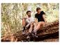 Koppel in sportieve T-shirts en schoenen zittend op een boomstam in het bos.
