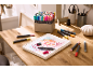 Een houten tafel met een schetsboek met bloemtekening en diverse stiften.