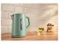 Mintgroene waterkoker met waterniveau-indicator op een houten aanrecht, met muntthee op de achtergrond.