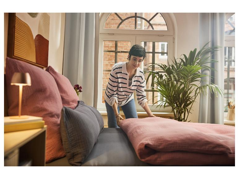 Vrouw maakt bed op met roze beddengoed en grijze en roze kussens.