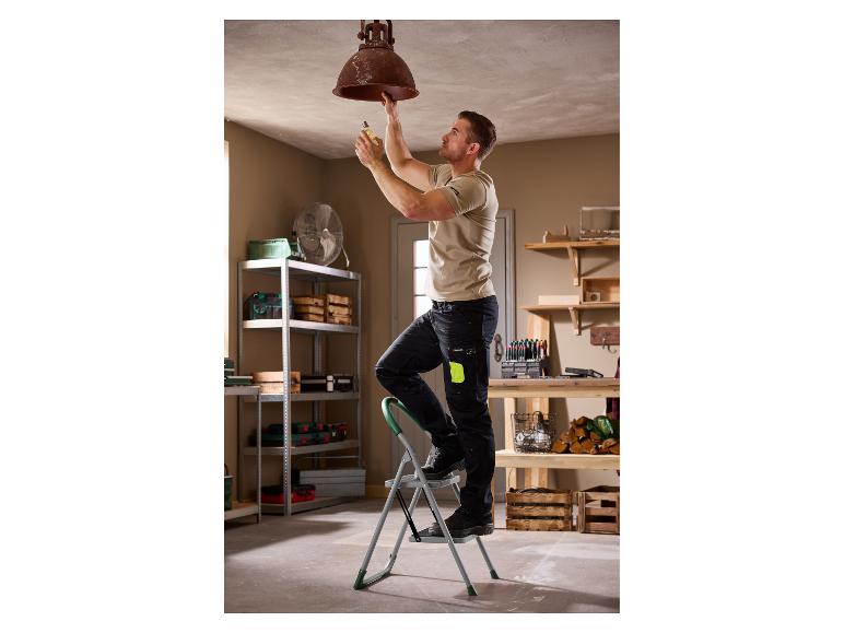 Man op ladder vervangt gloeilamp in plafondlamp in werkplaats.