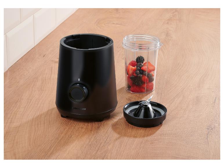 Zwarte blender met beker vol bessen en mes op een houten aanrecht.
