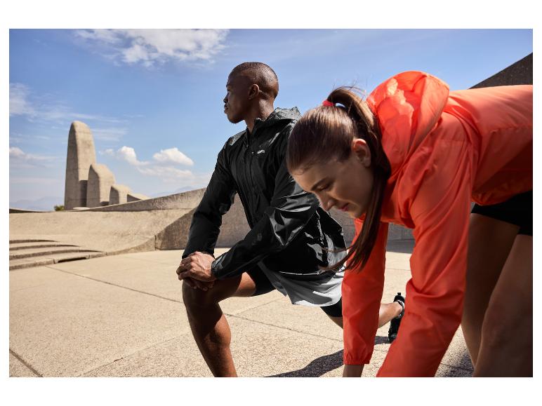 Twee atleten in sportkleding rekken buiten, met een monument op de achtergrond.