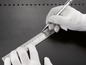 Een hand met een witte handschoen gebruikt een metalen liniaal en een pen om te meten.