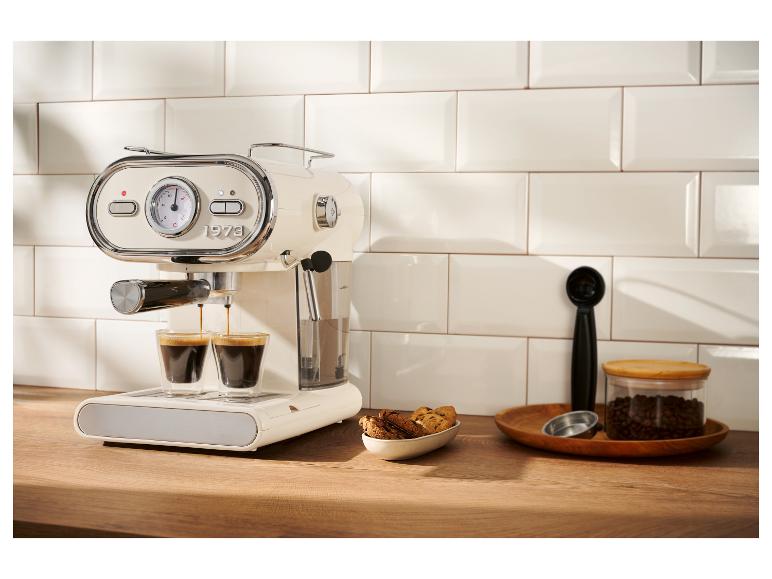 Een retro-stijl crèmekleurige espressomachine die koffie zet in twee kleine glazen op een houten aanrecht.