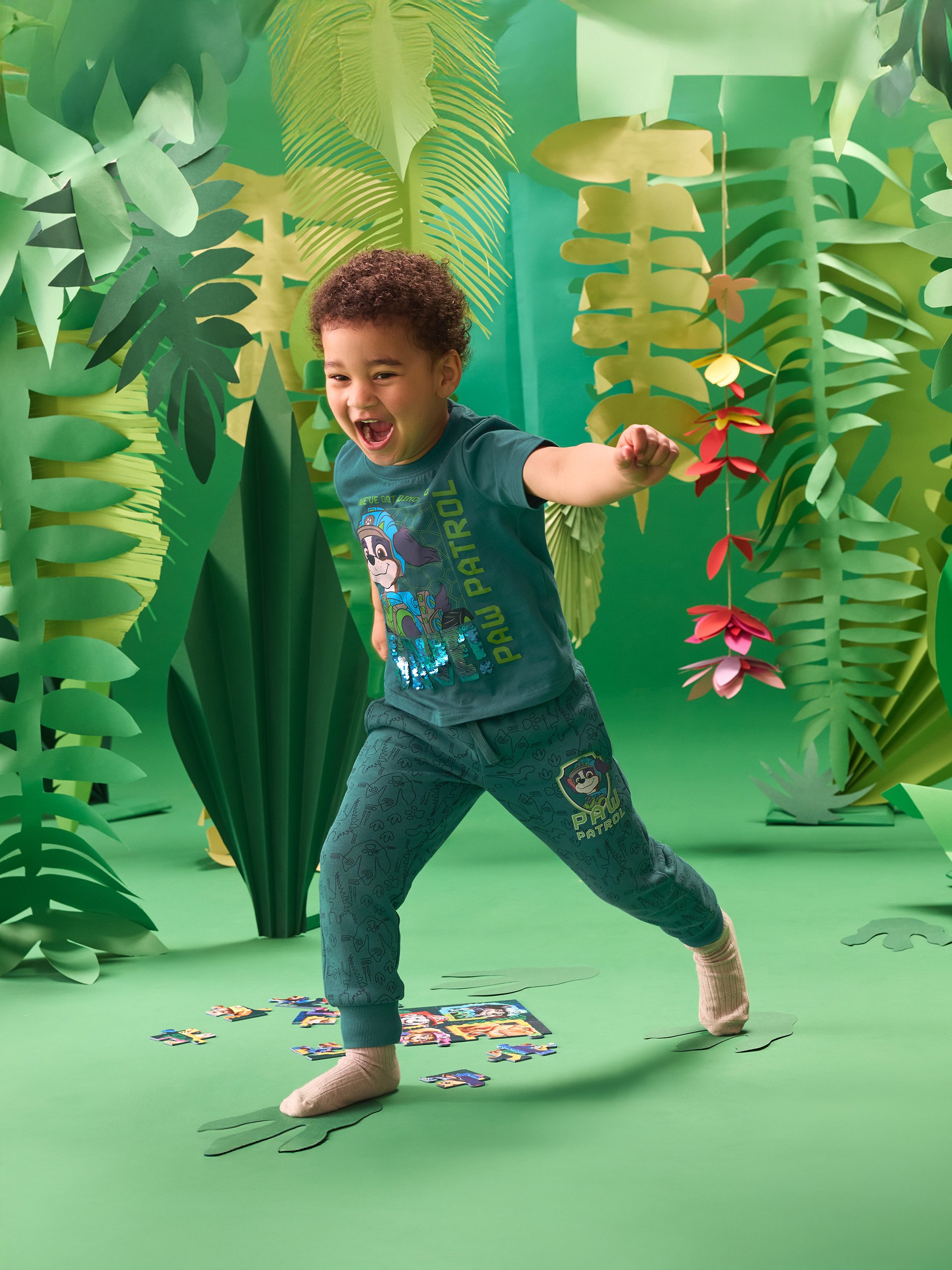 Peuterjongen in groen jungle-thema T-shirt en joggingbroek, spelend met een puzzel.