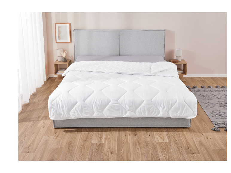 Een wit, gewatteerd dekbed op een grijs bed in een moderne slaapkamer.