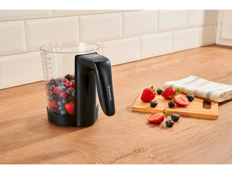 Blenderkan gevuld met bessen op een aanrecht, met gesneden aardbeien ernaast.