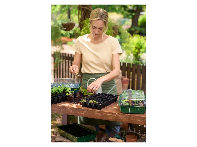 Vrouw plant zaden in kweekbakken en PARKISDE minikasjes in de tuin.