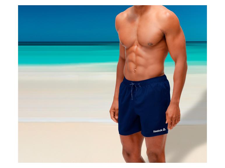 Man in donkerblauwe zwemshort op het strand.