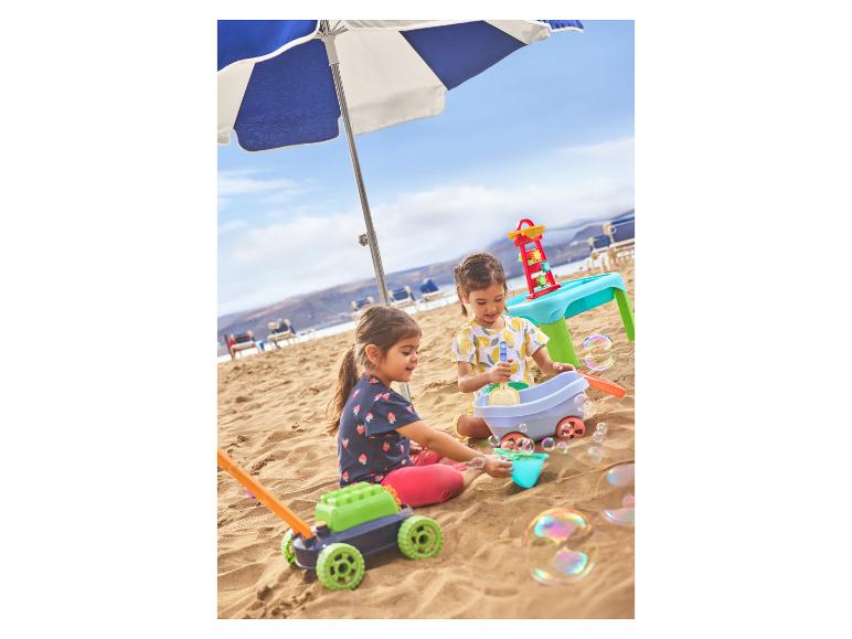 Twee kinderen spelen met zandspeelgoed en een bellenblaasmachine op een zandstrand.