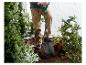 Persoon gebruikt een tuinschep om in de aarde te graven, omringd door planten en bloemen.