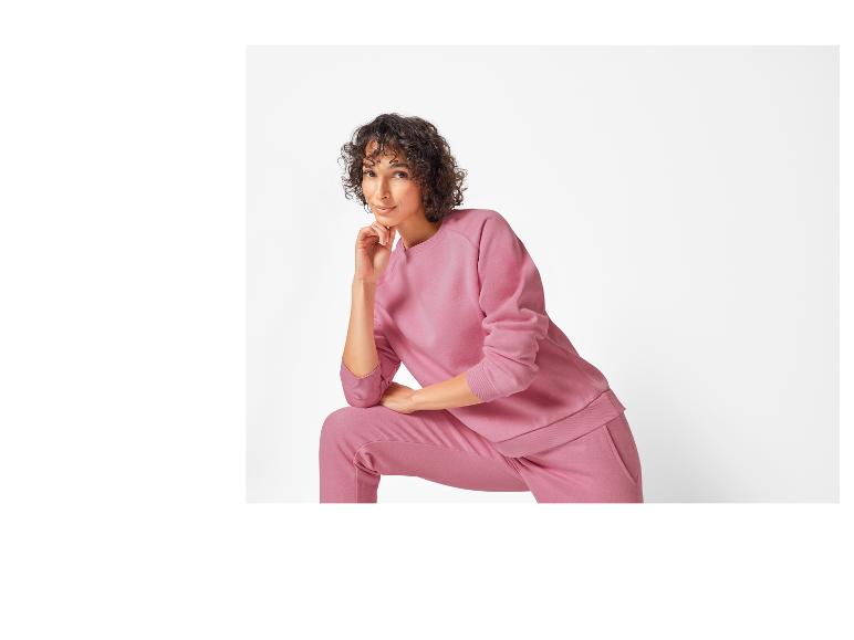 Een vrouw draagt ​​een roze hoodie en broek.