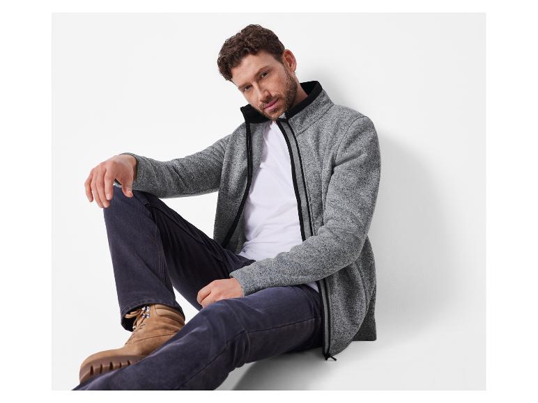 Man in grijs fleecejack, wit T-shirt en donkere jeans.